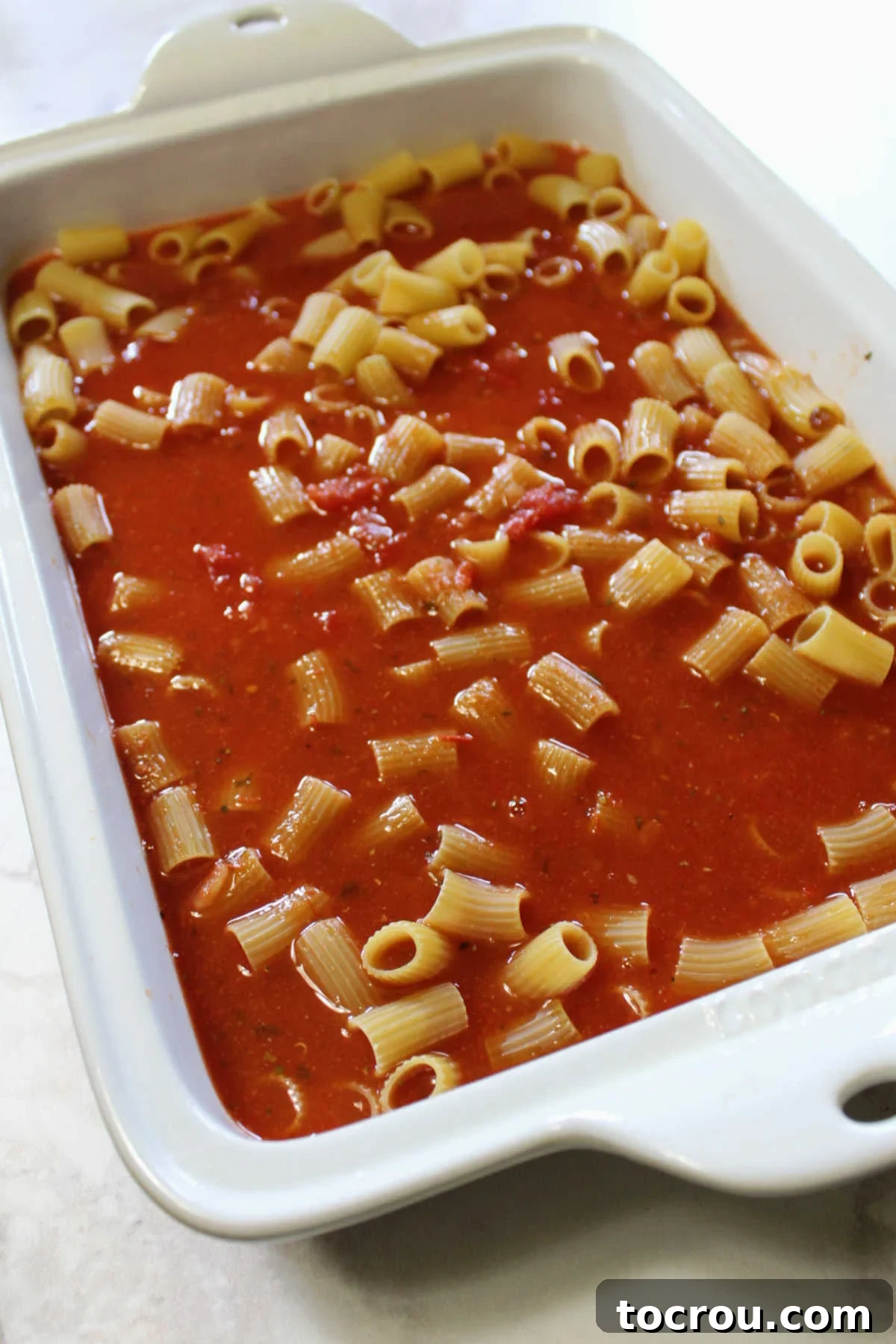 uncooked pasta and tomato sauce in baking dish ready for oven.