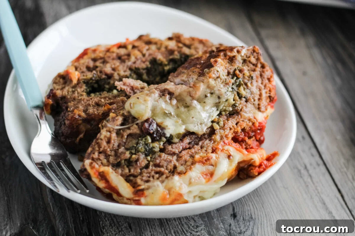Plate with two slices of meatloaf with melted cheese and pesto inside, topped with marinara sauce and more melted mozzarella cheese.