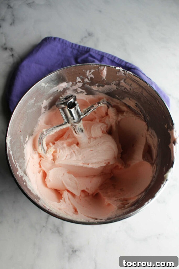 Mixer bowl filled with pink lemon frosting, showing its creamy texture.