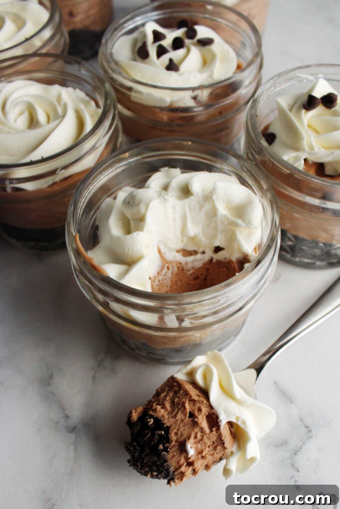 Small Ball jars showcasing layers of no-bake chocolate cheesecake and whipped cream, with one spoonful revealing the distinct layers.