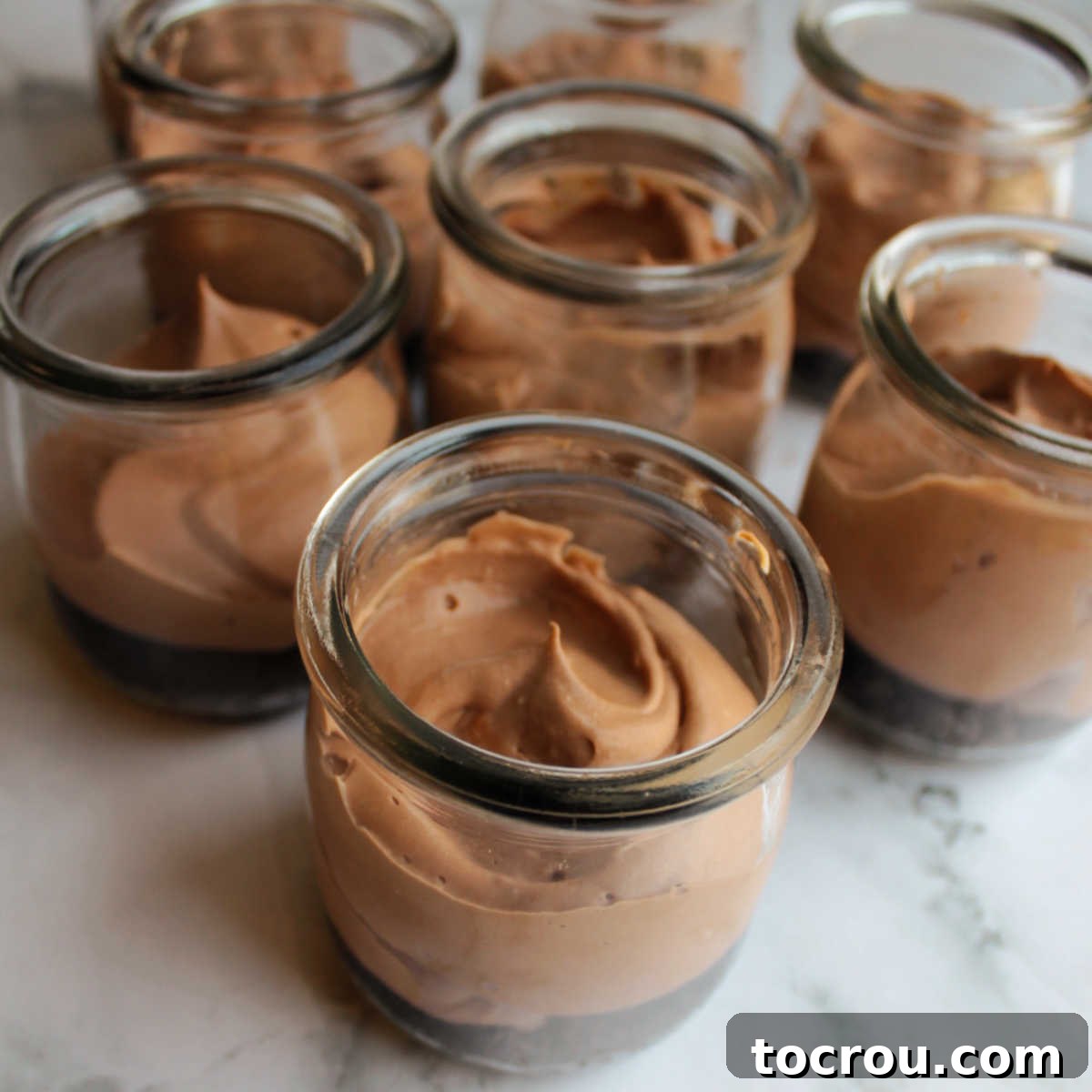 Overhead view into glass jars, showing the smooth, dark surface of the chocolate cheesecake filling settled over the crust.
