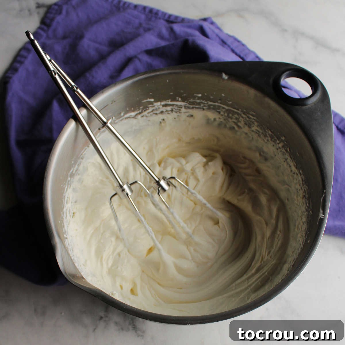 A mixing bowl filled with light, fluffy cream cheese whipped cream, with mixer beaters resting in the mixture.