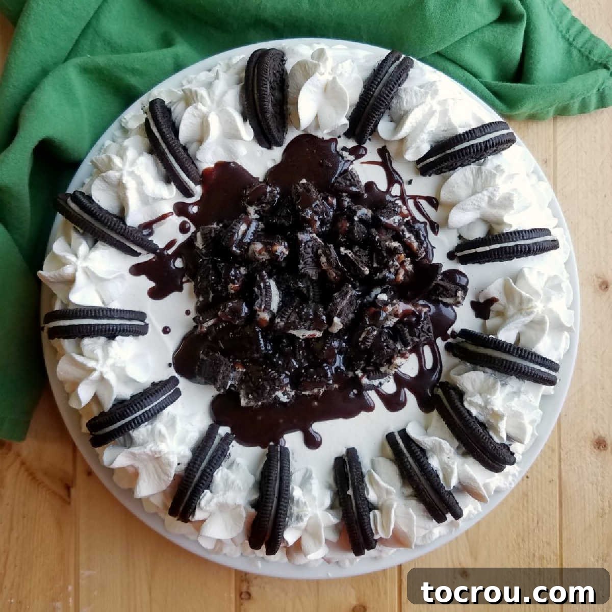 Delicious homemade ice cream crunch cake topped with chopped Oreos, a rich fudge drizzle, and fluffy whipped cream, ready to serve.