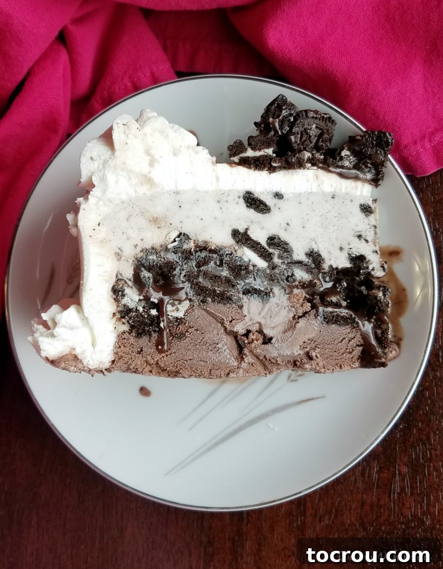 A perfectly sliced portion of homemade ice cream cake, showcasing the distinct layers of creamy ice cream and the decadent fudgy cookie crunch in the middle.