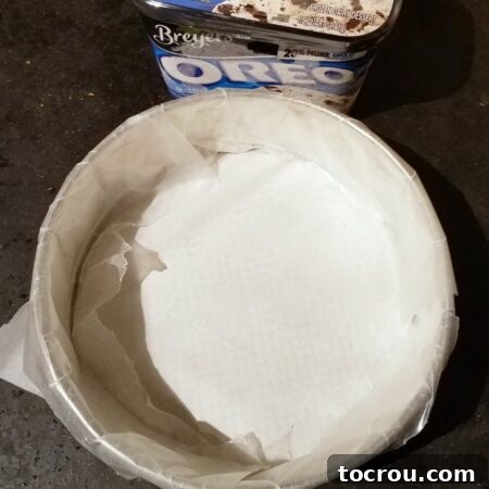 A springform pan lined with wax paper, with a quart of ice cream nearby, ready for the first layer.
