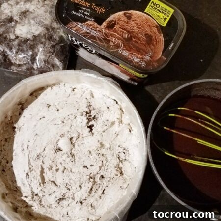 The first layer of ice cream spread in the pan, with additional ingredients like another quart of ice cream, fudge sauce, and crushed cookies nearby.