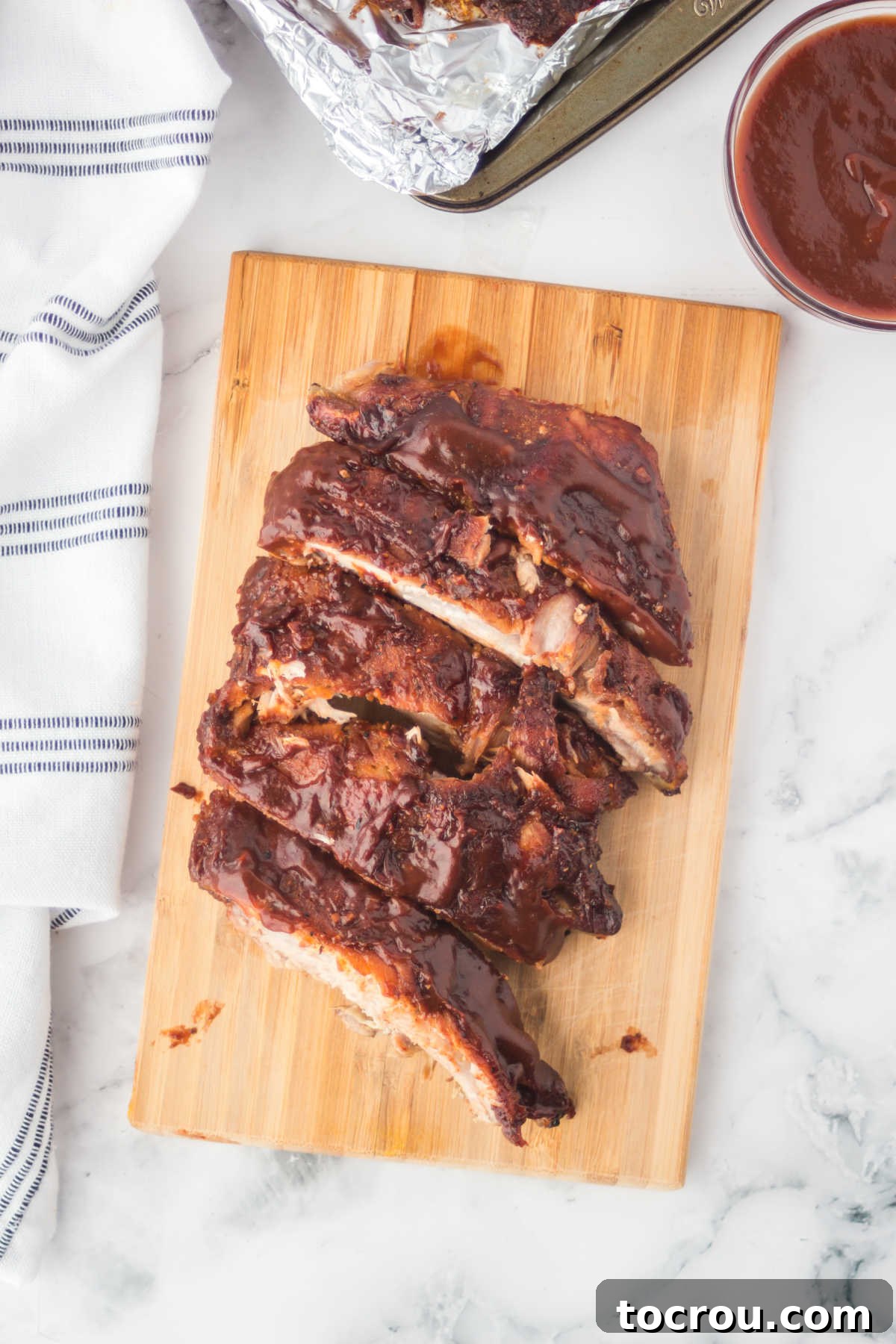 Mouthwatering Oven Baked Ribs 6 BBQ sauce coated ribs on wood cutting board.