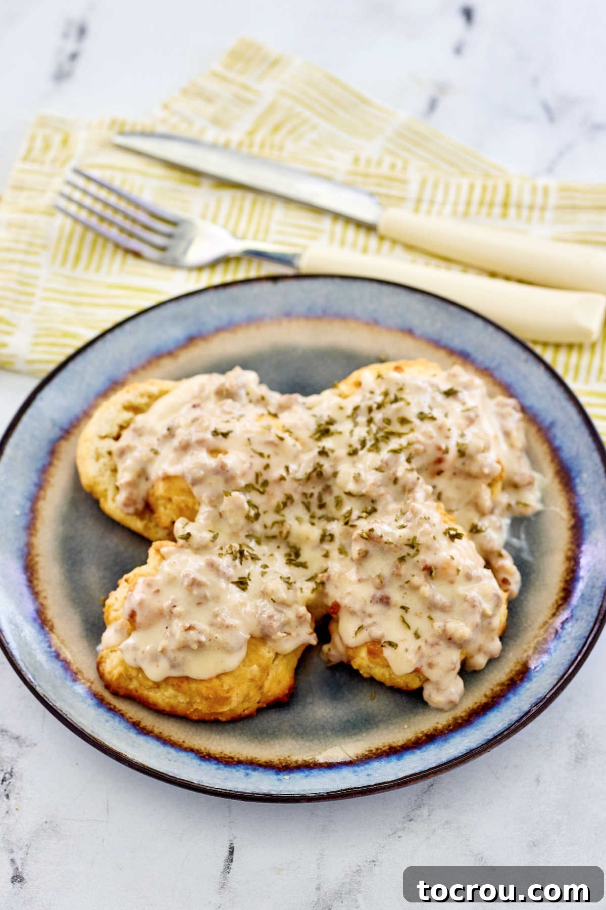 Fluffy Biscuits and Rich Sausage Gravy 3 A plate showcasing perfectly golden-brown biscuits generously topped with a rich, creamy milk gravy, featuring numerous savory crumbles of breakfast sausage.