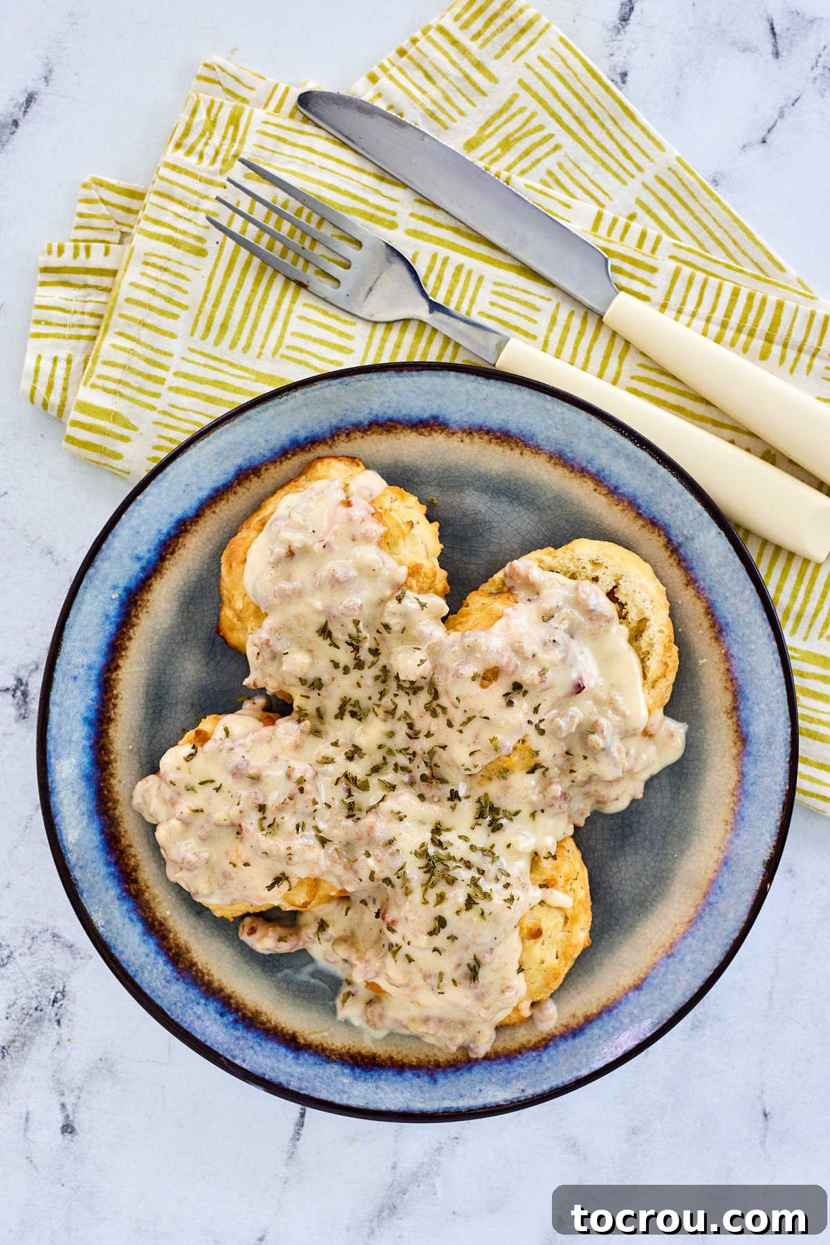 Fluffy Biscuits and Rich Sausage Gravy 8 A breakfast plate piled high with fluffy homemade biscuits and generous dollops of creamy gravy, accompanied by a fork and knife, inviting one to dig in.