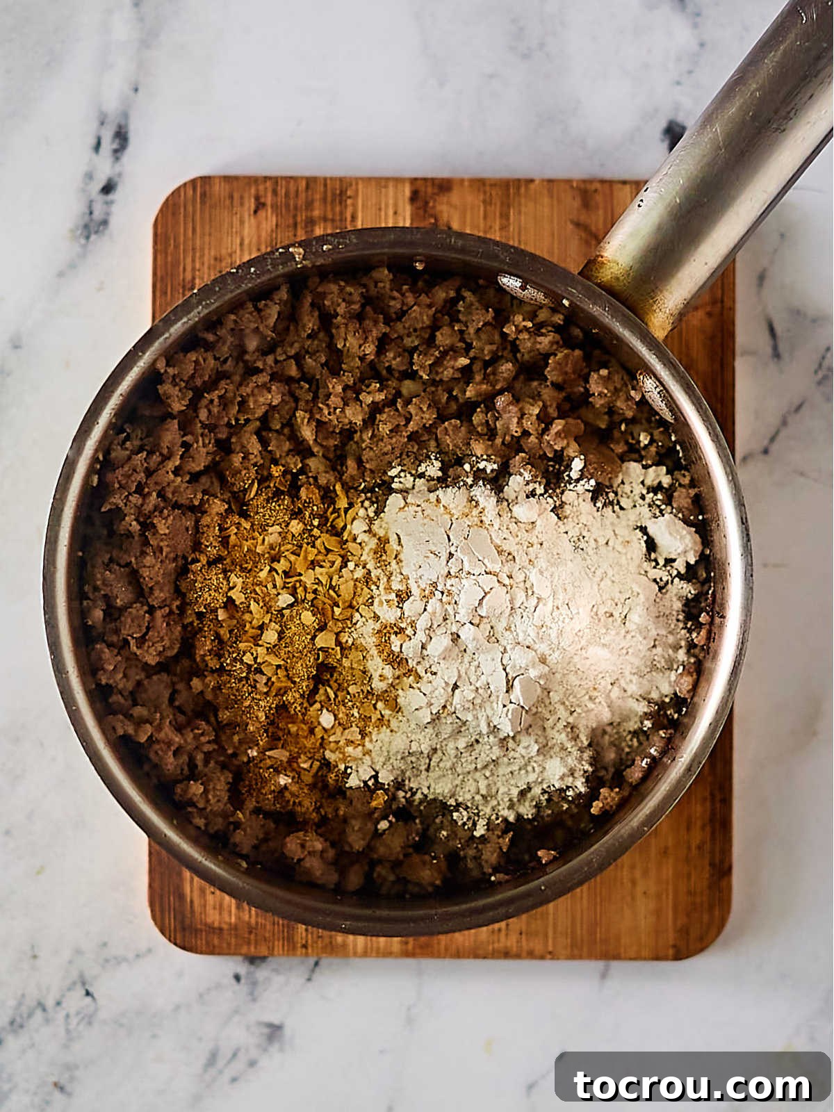 Fluffy Biscuits and Rich Sausage Gravy 9 A skillet containing browned breakfast sausage mixed with seasonings and flour, forming the base of a roux.