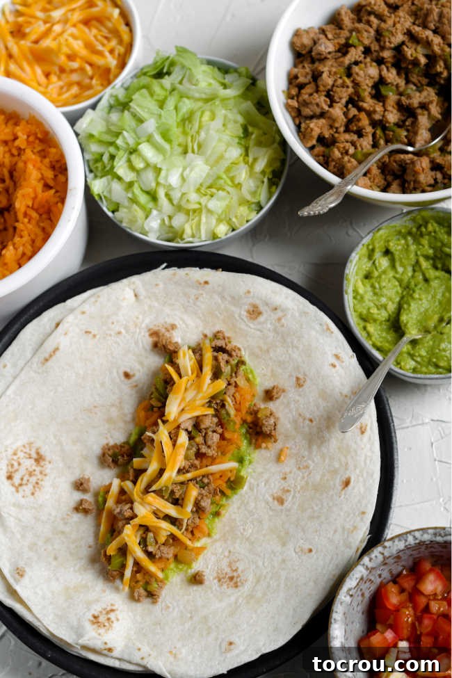 Assembling ground turkey burritos with meat and cheese on tortilla and all of the other toppings nearby.