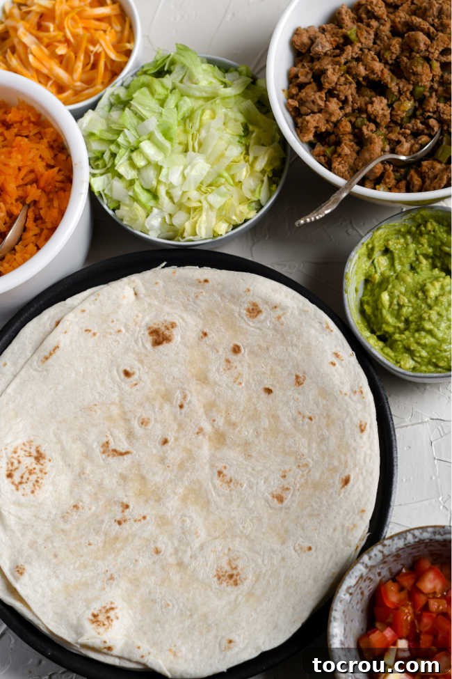 Burrito making ingredients including tortillas, shredded lettuce, guacamole, rice, cheese, seasoned ground turkey, tomatoes and more.