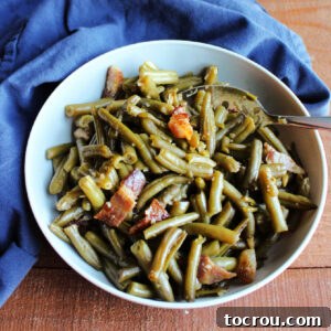 Homestyle Slow Cooker Smothered Green Beans 7 Serving bowl filled with shiny green beans and bacon smothered in sweet and sour sauce ready to eat.