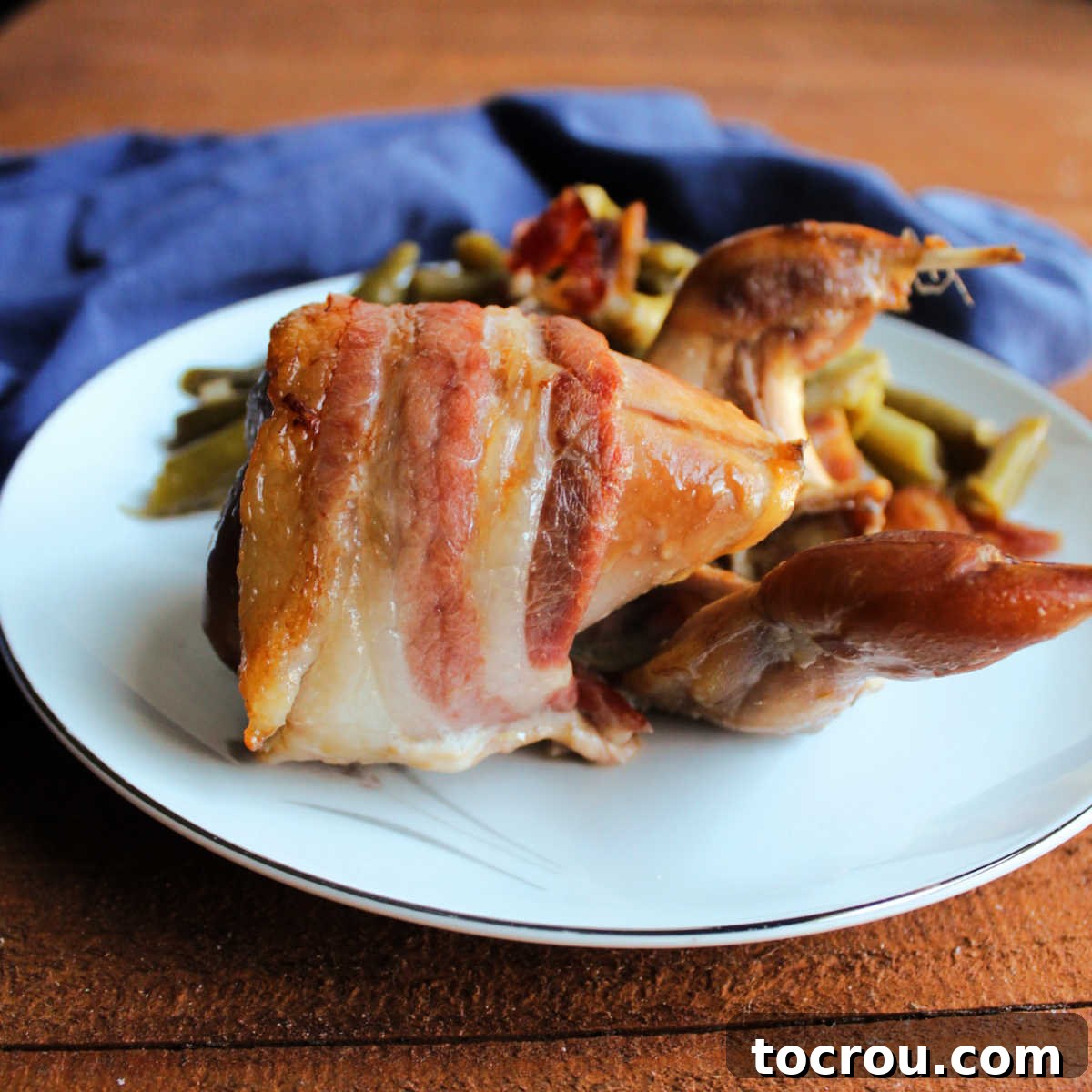 Golden Roasted Bacon Wrapped Quail 2 Roasted quail with bacon wrapped around it on plate, ready to eat.