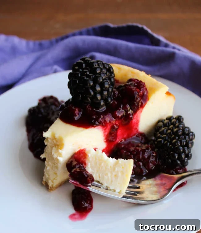 A serving of condensed milk cheesecake topped with vibrant blackberry sauce and fresh blackberries, ready to be enjoyed.