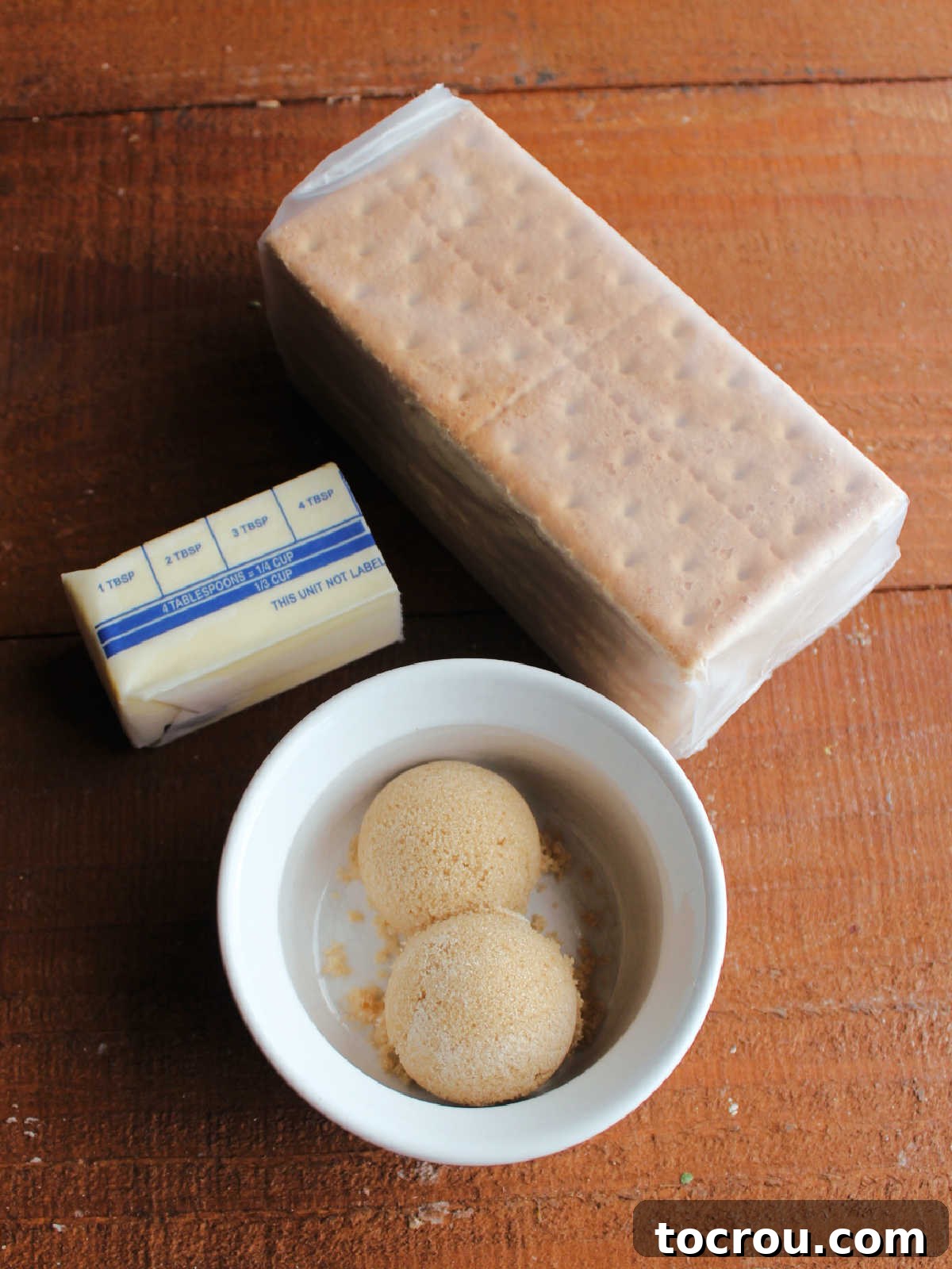 Crust ingredients including graham crackers, butter, and brown sugar laid out on a wooden surface.