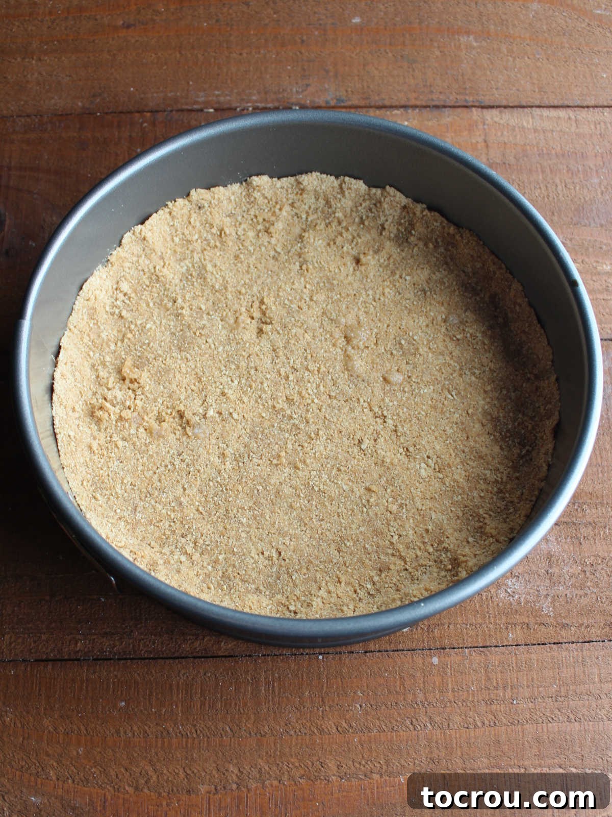 Grahame cracker crust evenly pressed into the bottom of a springform pan, ready for baking.