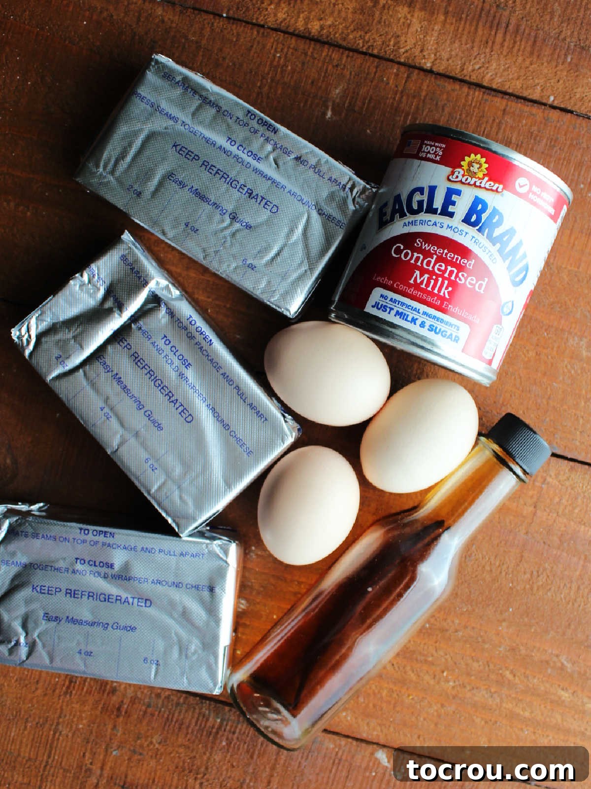 Ingredients including cream cheese, eggs, condensed milk, and vanilla, neatly arranged for making cheesecake batter.