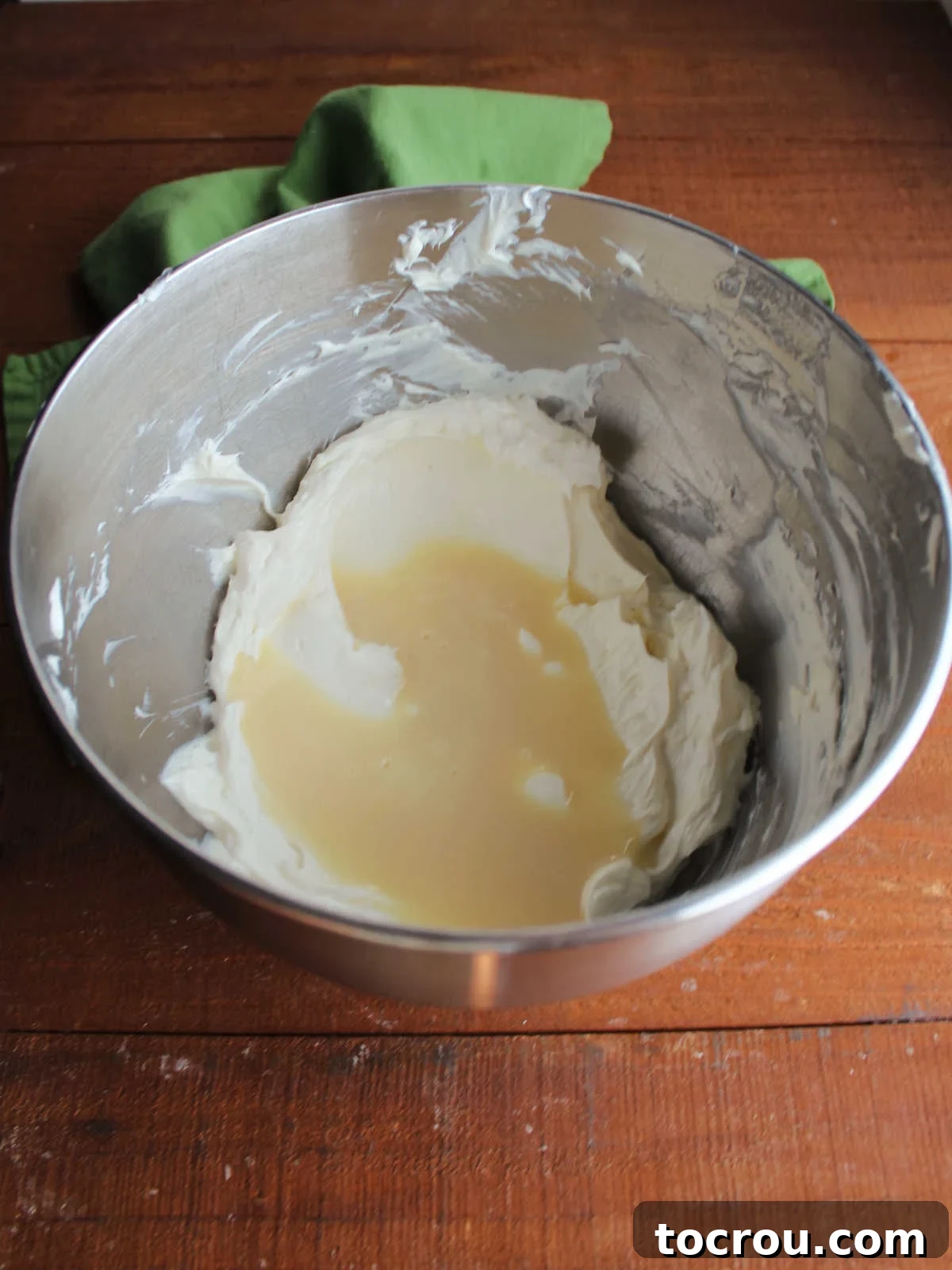 Mixer bowl containing beaten cream cheese and some condensed milk, midway through mixing for the cheesecake batter.