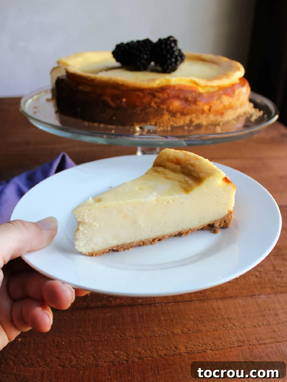 A perfectly sliced piece of creamy cheesecake on a plate, with the remaining cake visible in the background.