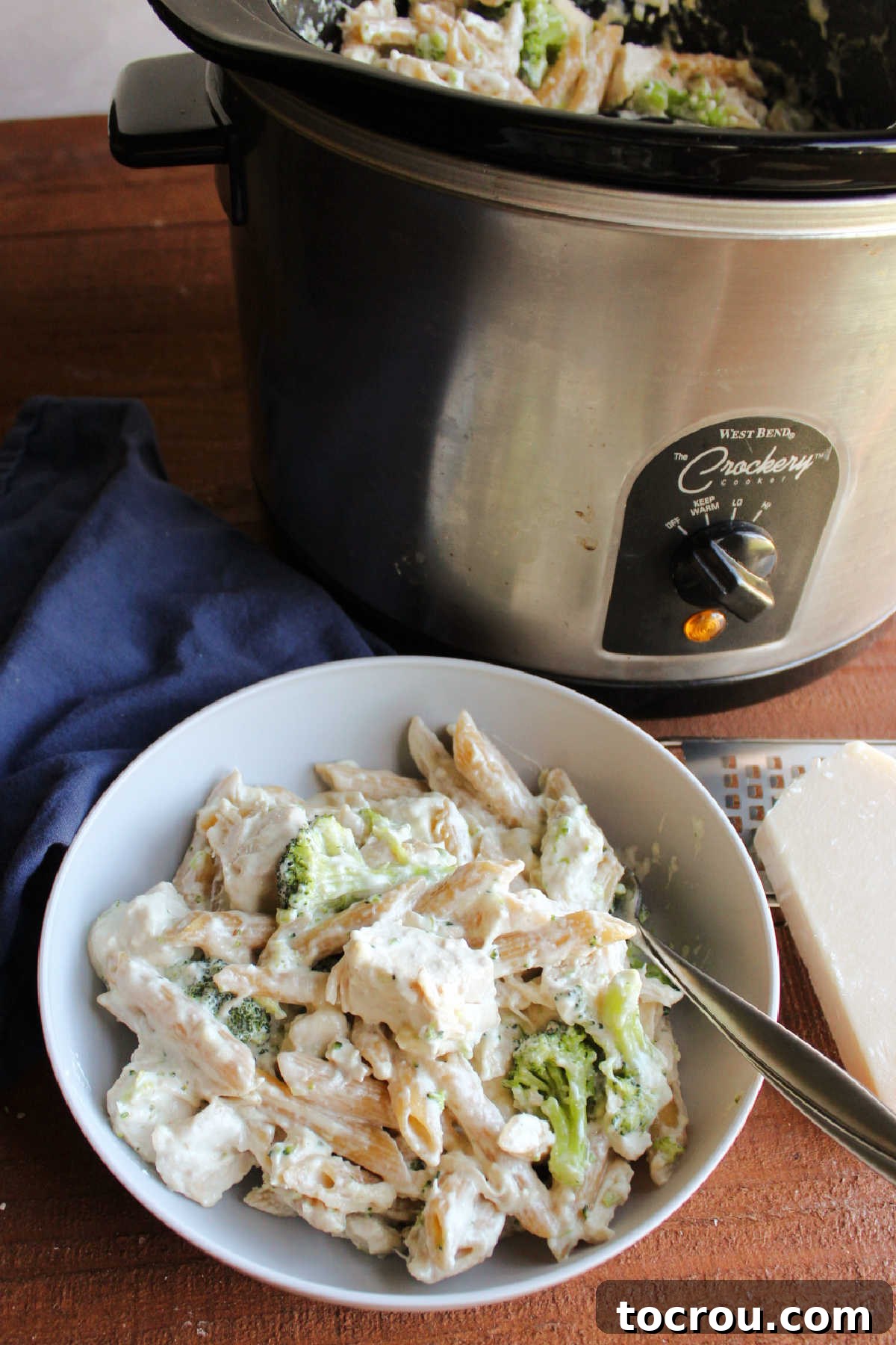A top-down view of the slow cooker brimming with rich, creamy chicken alfredo, featuring penne pasta, tender chicken pieces, and vibrant broccoli, ready to be served.