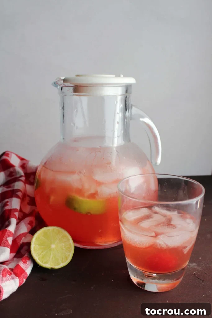 Cherry Limeade Glass and Pitcher Close-up of a glass of pink cherry limeade with ice, a cherry, and a lime slice, in front of a pitcher of homemade cherry limeade.