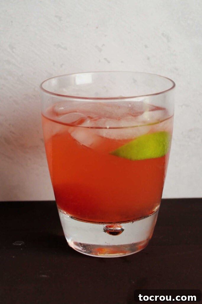 Cherry Limeade Glass Garnish A close-up of a glass of pink cherry limeade, garnished with a single maraschino cherry and a slice of fresh lime.