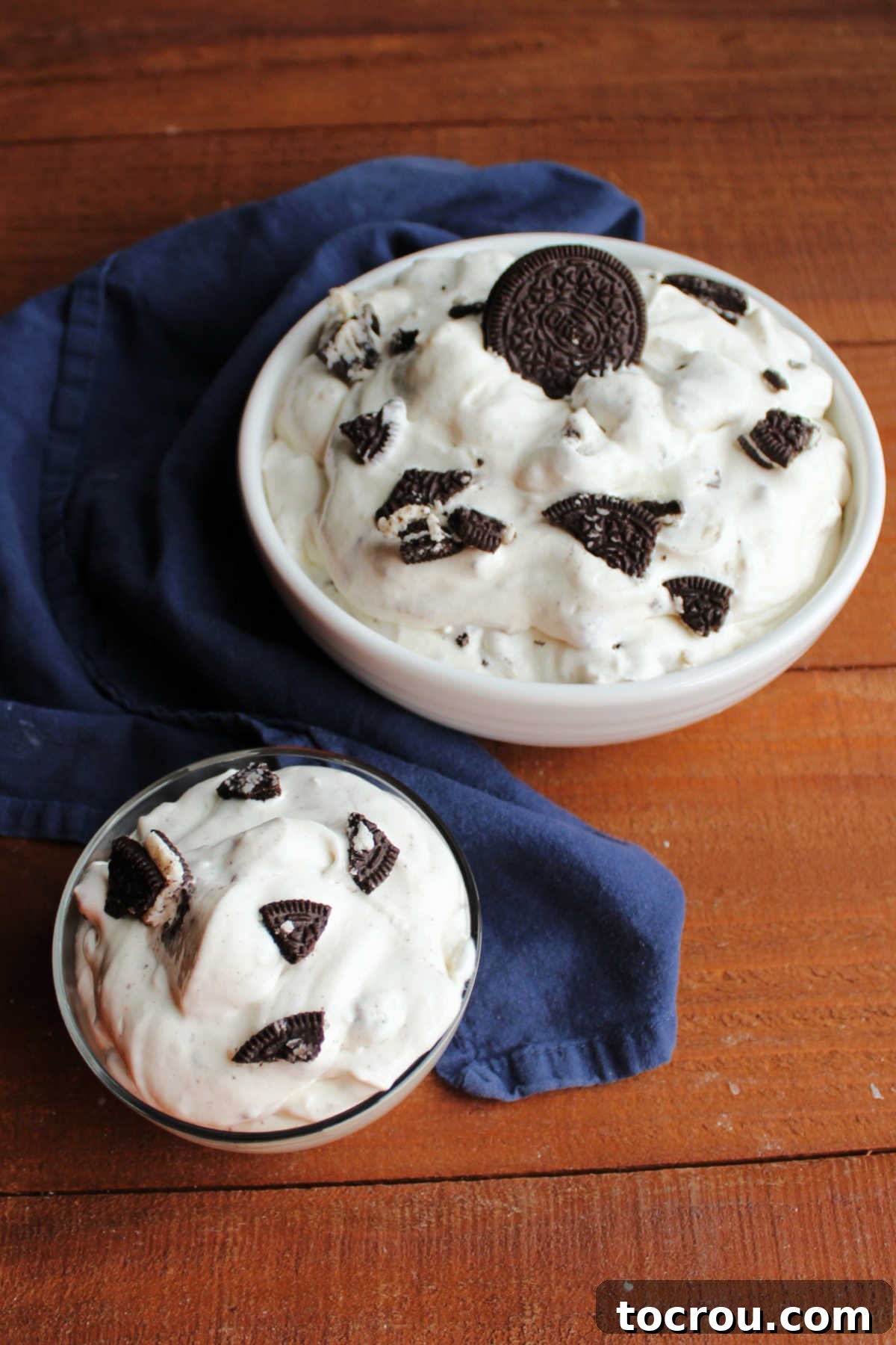 Oreo Fluff Ready to Serve A large serving bowl filled with Oreo fluff dessert, with a smaller individual portion scooped into a clear glass dish next to it. The texture is creamy and smooth, adorned with visible cookie pieces.