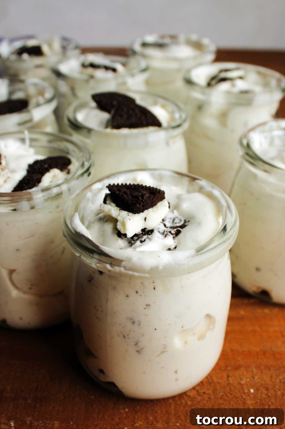 Finished Oreo Fluff in Jars Close-up shot of individual clear jars filled with the creamy white Oreo salad dessert, showcasing the mixed-in cookie pieces. The jars are lined up neatly, ready for serving.