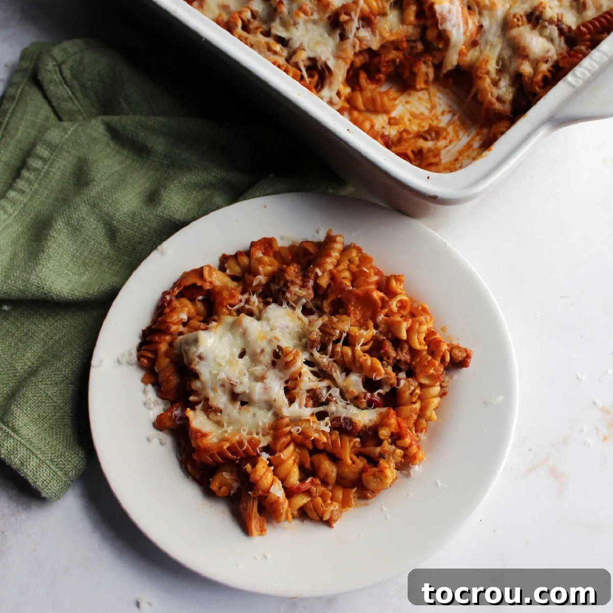 Plate of no boil pizza pasta bake next to casserole dish, showing melted cheese and rich sauce.