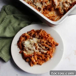 Plate of no boil pizza pasta bake next to casserole dish, showcasing a perfect serving.