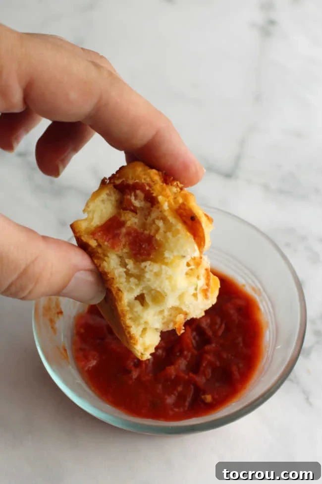 Dipping pizza muffin into marinara Close-up of a hand gracefully dipping a savory piece of a pepperoni pizza muffin into a small, pristine white bowl of rich marinara sauce, highlighting the perfect texture.