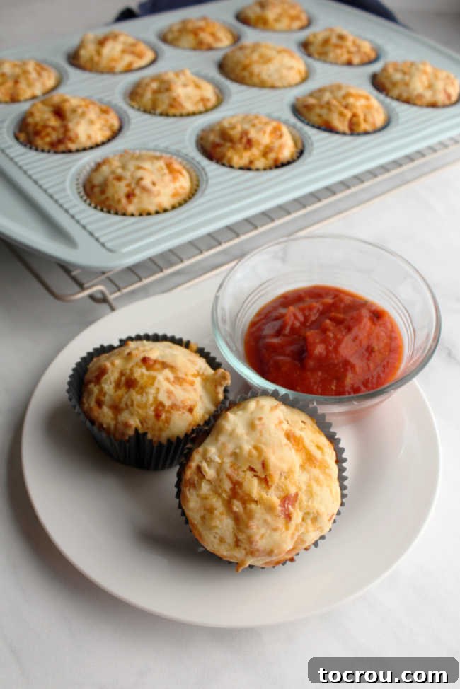 Pizza muffins and marinara sauce on a plate A beautifully arranged plate featuring several pepperoni pizza muffins and a small, inviting bowl of marinara sauce, all ready to be served and enjoyed.