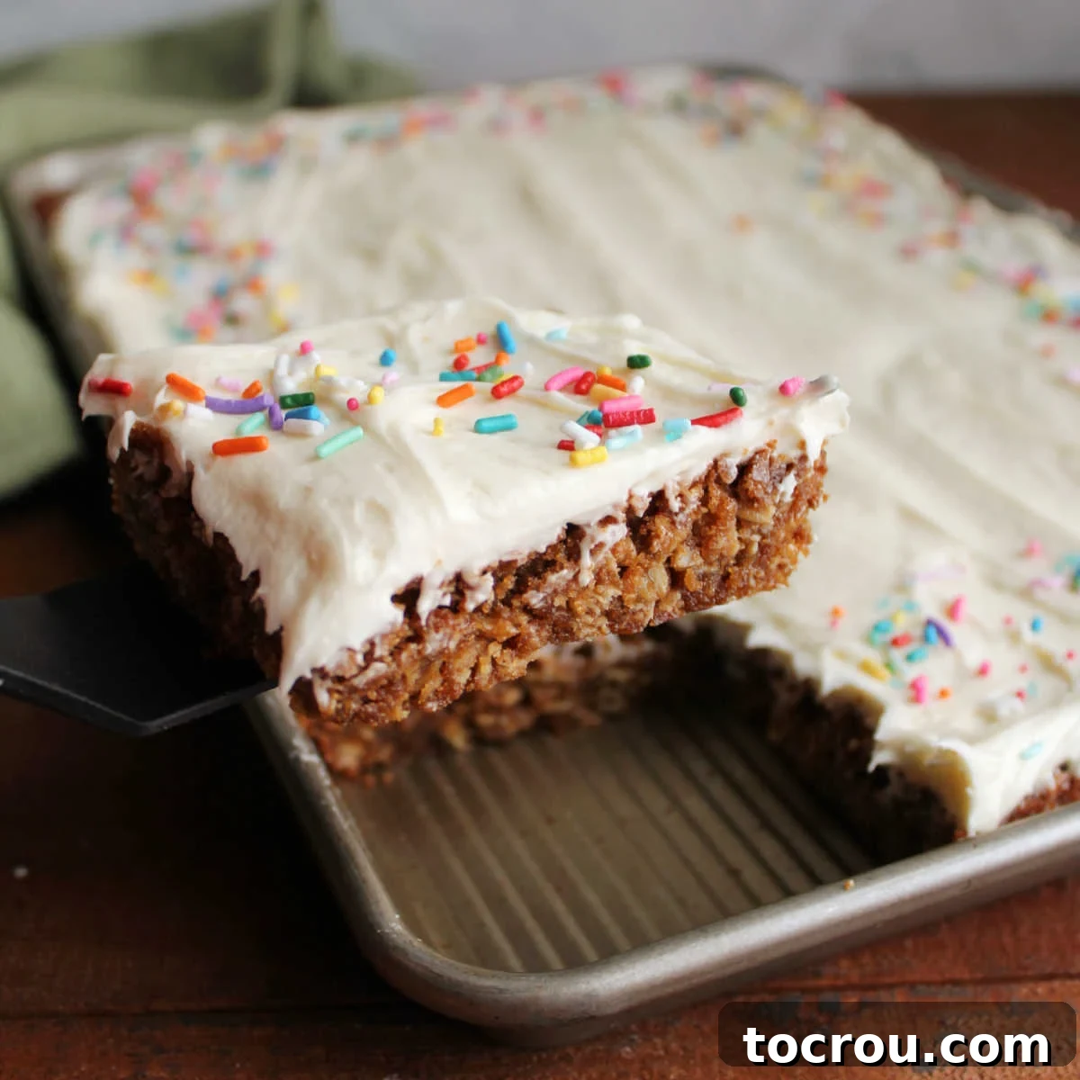 Spatula lifting out first square of oatmeal cream pie bars with chewy molasses and oatmeal cookie layer topped with fluffy white marshmallow fluff buttercream and sprinkles. 