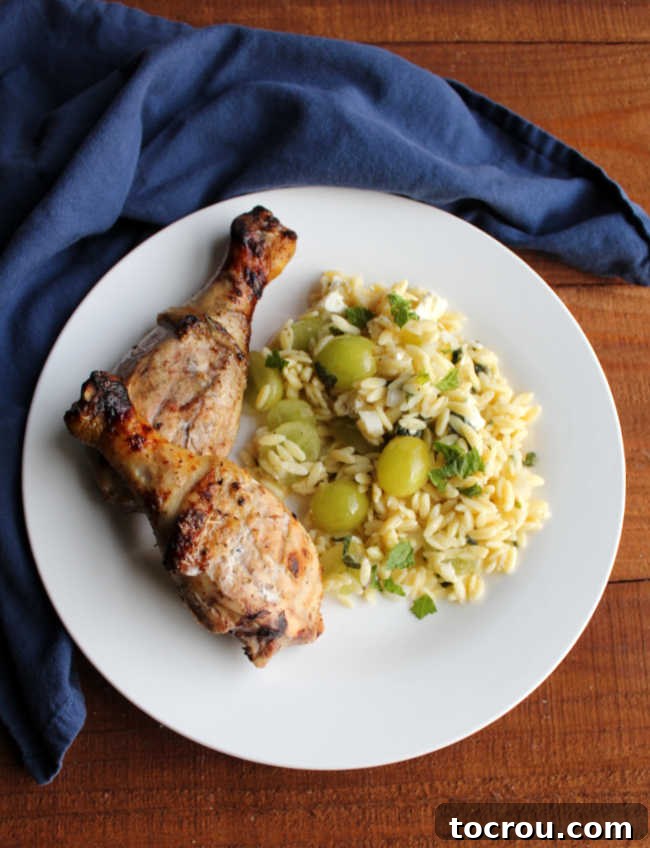 Grilled Chicken with Mediterranean Orzo Salad A beautifully arranged plate featuring grilled chicken legs and a refreshing grape orzo salad, creating a complete and inviting meal.