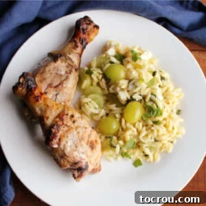 Grilled chicken drumsticks arranged on a plate next to a fresh orzo pasta salad, beautifully presented and ready to be enjoyed.