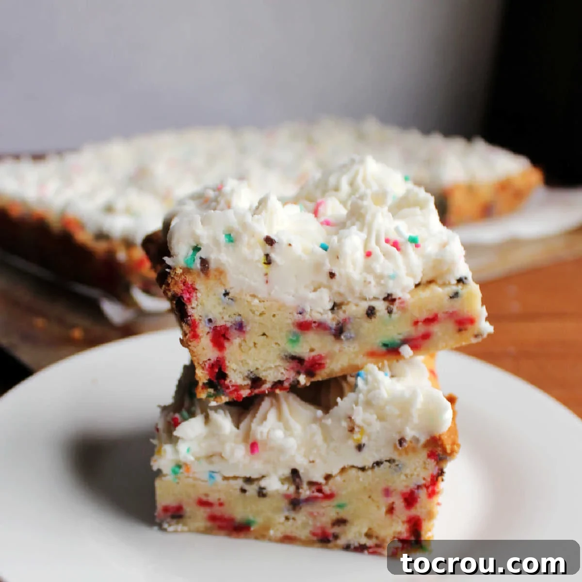 Party Sugar Cookie Bars 2 Two thick soft frosted sugar cookie bars with lots of sprinkles stacked on top of each other, showcasing their vibrant colors and fluffy frosting.