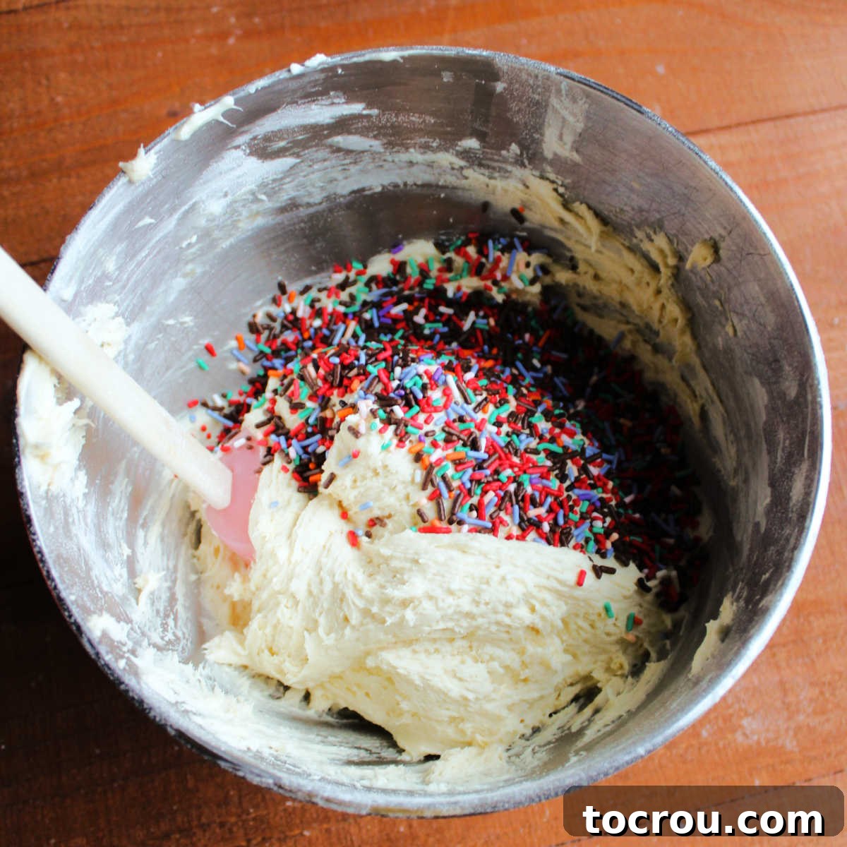Party Sugar Cookie Bars 3 Sugar cookie dough and a cup of colorful sprinkles in a mixing bowl, ready to be combined for a festive treat.