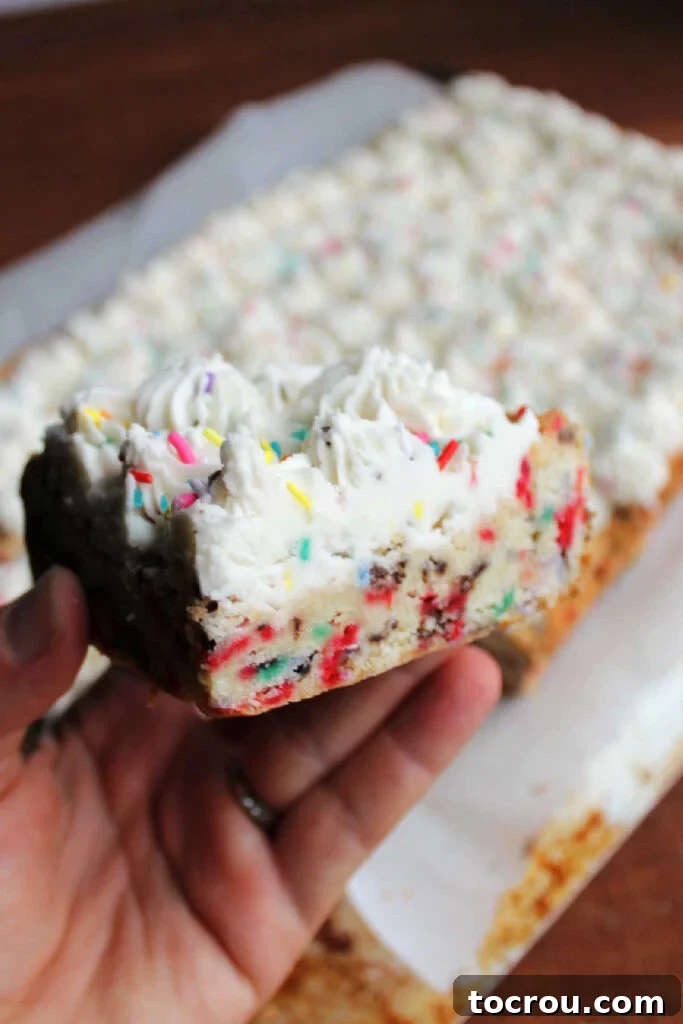 Party Sugar Cookie Bars 7 A hand holding a beautifully frosted soft sugar cookie bar, showcasing the vibrant colorful sprinkles baked inside and on top of the buttercream.
