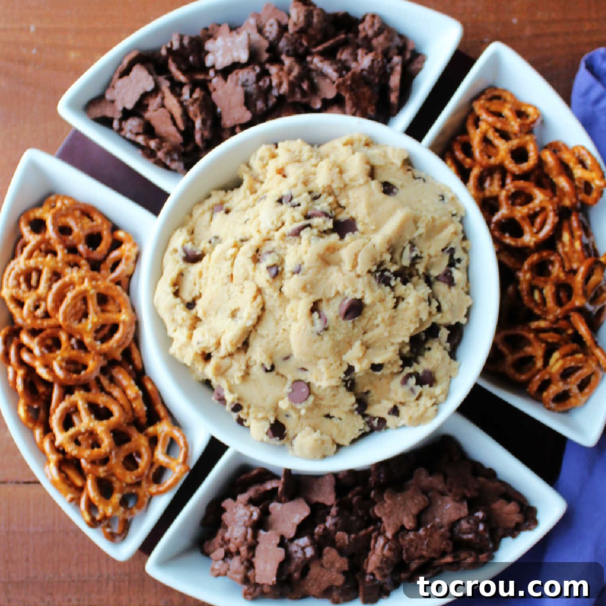 Irresistible Chocolate Chip Cookie Dough Dip with Dippers A chip and dip server showcasing a generous portion of chocolate chip cookie dough dip in the center, surrounded by an array of dippers including crunchy pretzels and sweet chocolate teddy grahams.