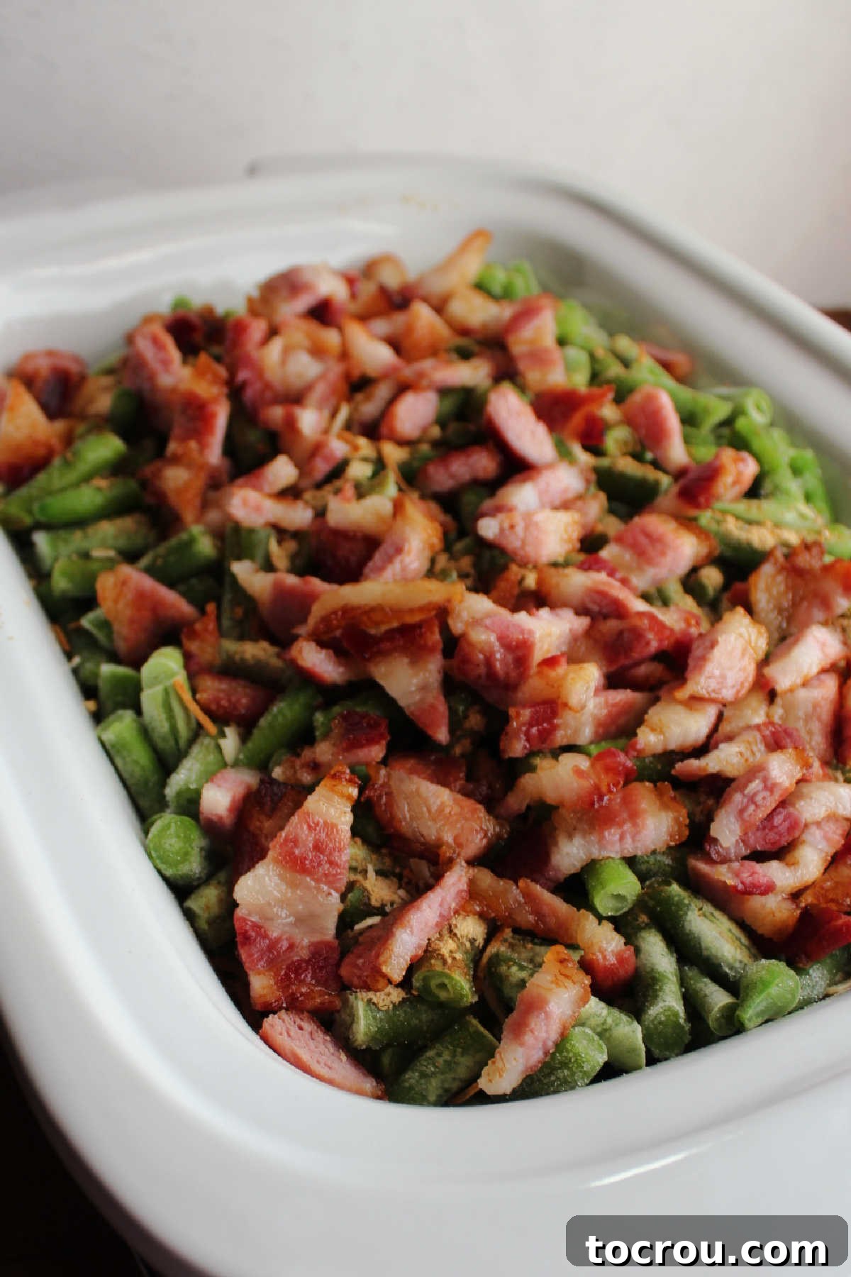 Lots of big bacon pieces over green beans in slow cooker.