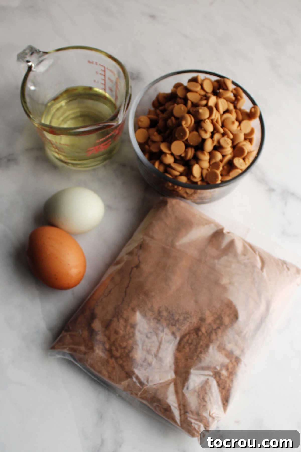 Essential ingredients for easy cake mix cookies: a box of chocolate cake mix, eggs, cooking oil, and a bag of peanut butter chips laid out on a clean surface.