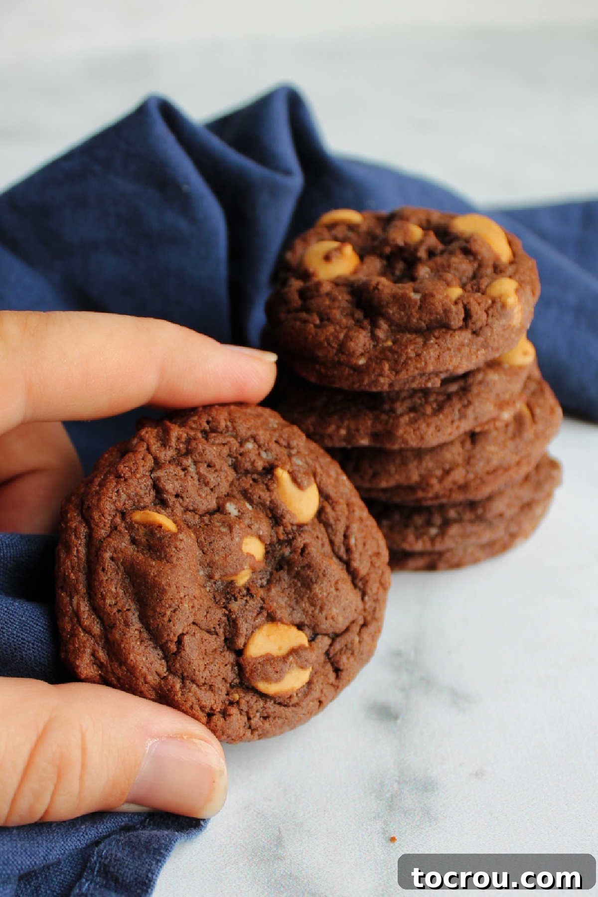 A hand holding a soft, perfectly baked chocolate cookie adorned with melted peanut butter chips.