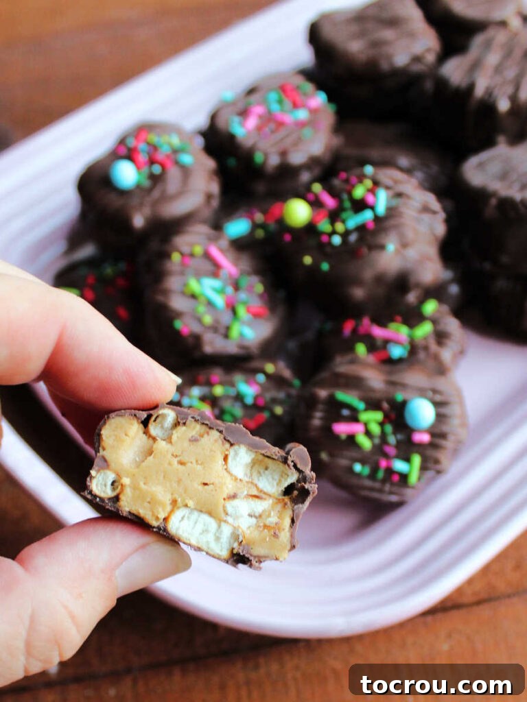 Decadent Chocolate Peanut Butter Pretzel Treats 3 A hand holding a perfectly split chocolate peanut butter pretzel bite, revealing the thick chocolate coating, creamy peanut butter filling, and the crunchy pretzel pieces within.