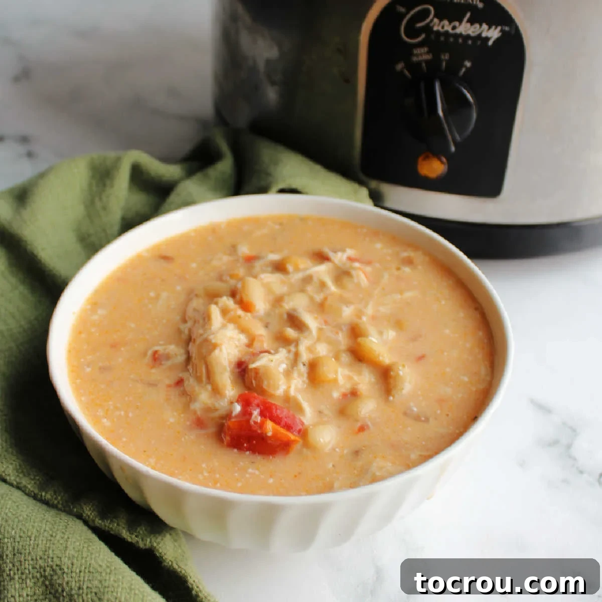 Delicious Creamy Buffalo Chicken Chili Bowl of creamy soup with white beans, chicken and bits of tomato showing in front of crock pot.