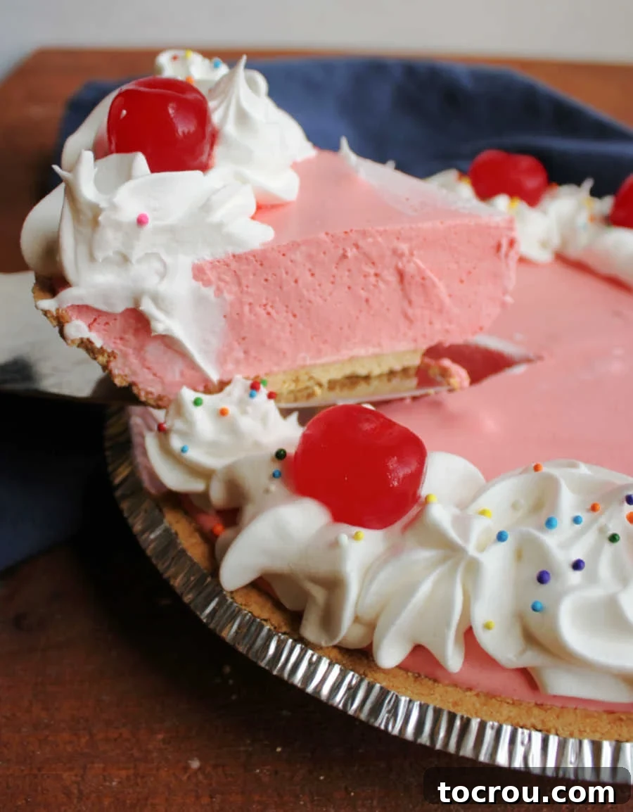 Lifting slice of cherry jello pie out of pie plate, showing its light and fluffy texture.