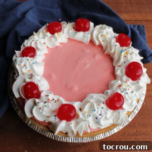Whole pink cherry jello pie with whipped topping piped around the edge and maraschino cherries on top.