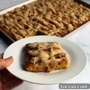 Hand holding dessert plate with a piece of peach sheet cake drizzled with brown butter glaze.