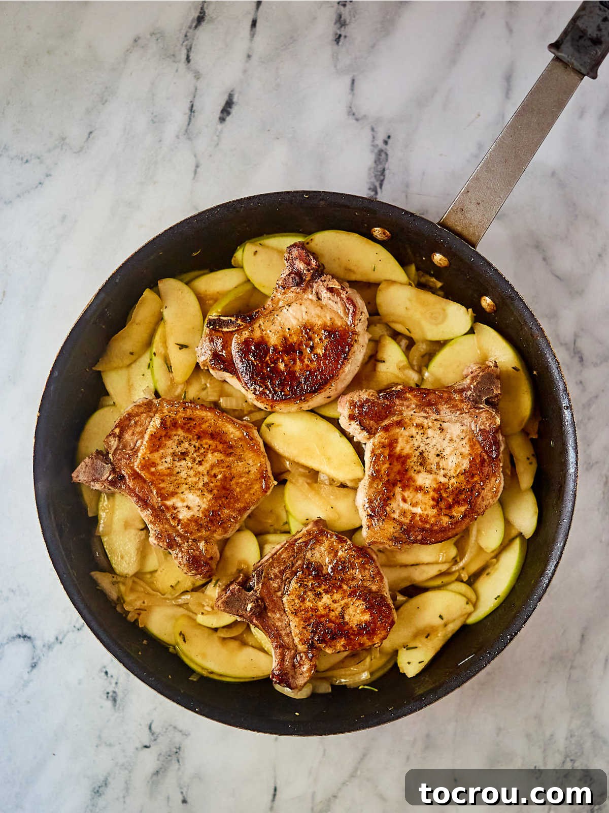 Skillet with perfectly cooked pork chops nestled into a savory-sweet mixture of apples and onions, prepared for plating.