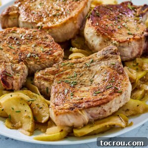 Platter with cooked apples topped with browned pork chops garnished with bits of rosemary.